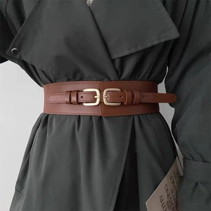 Dettaglio di un'ampia cintura in pelle marrone scuro con doppia fibbia dorata su un trench grigio