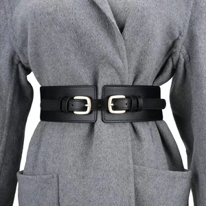 Cintura elastica nera da donna con doppia fibbia dorata su un cappotto grigio