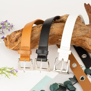 Close-up of three narrow faux leather belts with star embossed buckles on a wood branch