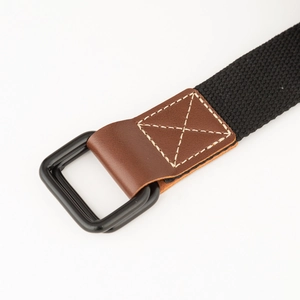 Detail van zwarte canvas riem met dubbele D-ring gesp en bruin lederen verbinding met stiksel