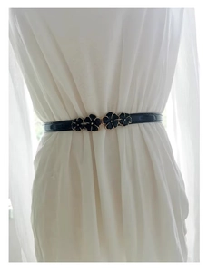 Detail of black patent leather skinny belt with floral buckle on white dress