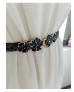 Detail of adjustable black patent leather skinny belt with black gold floral buckle