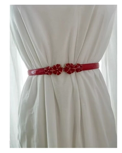 Detail of red patent leather skinny belt with a plum blossom floral buckle on dress
