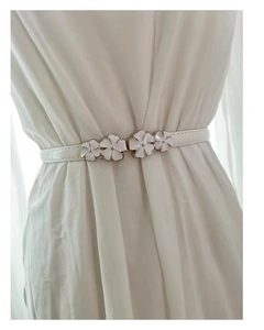 Detail of white floral buckle and thin leather belt on white pleated chiffon dress