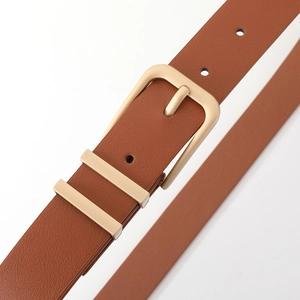 Detail of a slim brown leather belt with premium champagne gold pin buckle and double rings
