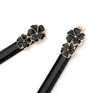 Close-up of black patent leather belt with golden-edged enamel flower buckle detail
