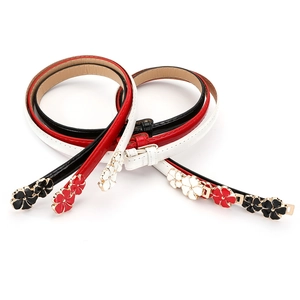 Close-up of three thin patent leather belts in black, red, and white with floral buckles
