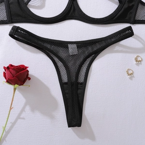 Detail of black mesh lingerie set with hollowed-out cups and thong on a white texture background