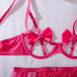Dettaglio del set lingerie in pizzo rosa con fiocchi e cinturini ritagliati su tessuto bianco
