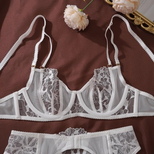 Close-up of white floral lace embroidery on sheer mesh lingerie set with gold adjusters