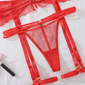 Détail de jarretière et string en dentelle rouge avec anneaux dorés sur drap blanc