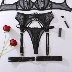 Flat lay of black floral lace lingerie set with gold buckles and red rose decor