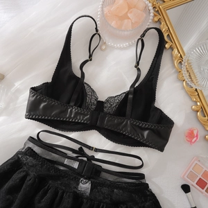 Flachliegendes schwarzes Spitzenunterwäsche-Set mit Strapsen und Metalldetails auf Weiß
