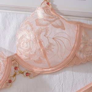 Détail de broderie florale sur soutien-gorge en dentelle rose avec chaîne dorée et gemme
