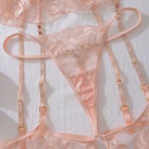 Détail d'un ensemble de lingerie en dentelle rose avec boucles dorées et bijoux rouges