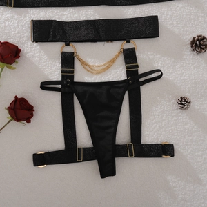 Detail view of black lingerie with golden metal chains and rings on white faux fur background