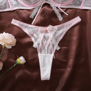 Détail de string en dentelle rose avec nœud et pendentif sur fond de satin brun