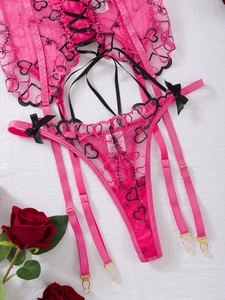 Detail of rose pink lace garter set featuring black heart embroidery and satin bows