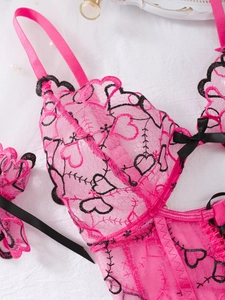 Macro detail of rose pink mesh lace with black heart embroidery and satin bow