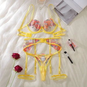 Flat lay of yellow lace embroidery bra set with garters, red roses, and pearls