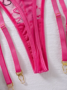 Detailed macro shot of hot pink lace embroidery and gold metal garter clips on lingerie