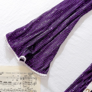 Macro detail of purple sequined fabric with white lace trim on a musical score background