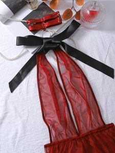 Detail of red mesh bodysuit featuring a large black satin bow and metal ring neck strap