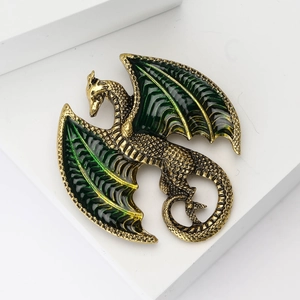 Detailed close-up of a golden dragon brooch with green enamel wings on white background