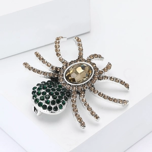 Detailed macro of a vintage silver spider brooch with amber crystal and green rhinestones