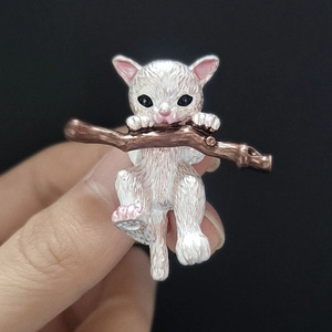 Detailed macro shot of white enamel cat brooch clinging to a metallic branch detail