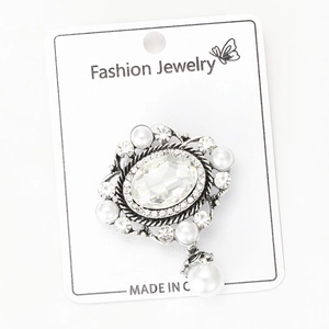Dettaglio di spilla vintage in vetro con perle e strass su un cartoncino espositivo
