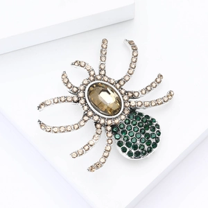 Close-up of spider brooch with large brown gemstone and green rhinestones on silver base