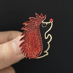 Detailed close-up of a hedgehog brooch with red pavé texture and golden metallic edges