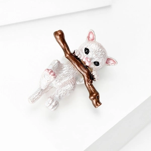 Detailed close-up of a cute white cat enamel brooch resting on a brown tree branch