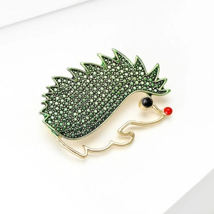Detail of hedgehog brooch with green crystals and golden alloy framing on white stand