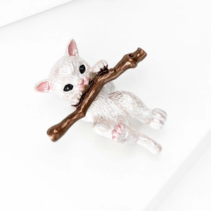 Detail of a white enamel cat brooch clutching a brown branch with a textured finish