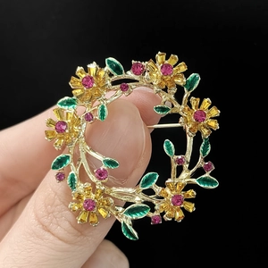 Detailansicht einer goldenen Blumenkranz-Brosche mit grüner Emaille und rosa Kristallen