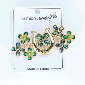 Detailed close-up of lucky horseshoe brooch with green clover flowers and Good Luck engraving