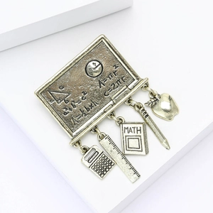 Detail of chalkboard brooch with mathematical formulas and small school-themed charms