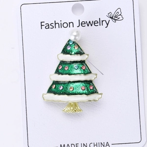 Close-up of a Christmas tree brooch with green enamel, rhinestones and a white pearl bead
