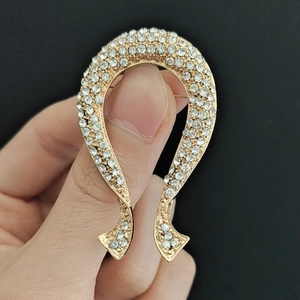 Détail d'une broche en forme de nœud doré ornée de strass brillants tenue par une personne