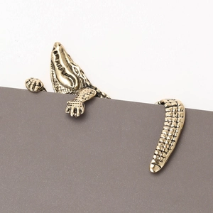 Detailed close-up of golden metal crocodile brooch with textured scales on grey card