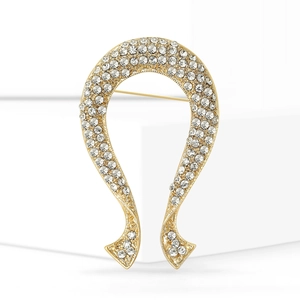 Détail d'une broche fer à cheval dorée avec strass scintillants sur un socle blanc