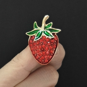 Close-up of strawberry brooch featuring red rhinestones and green enamel leaf detail