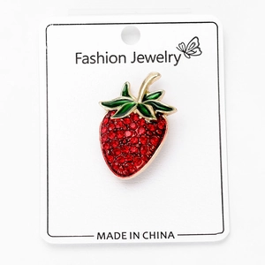 Macro detail of strawberry brooch with red rhinestones and green enamel on jewelry card
