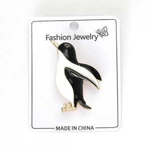 Détail de la broche pingouin en émail noir et blanc sur une carte de présentation
