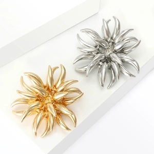 Artistic golden and silver firework-shaped alloy brooches displayed on white podiums