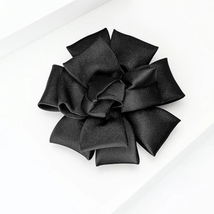 Detail of multi-layered black fabric camellia brooch with elegant ribbed texture on white stand