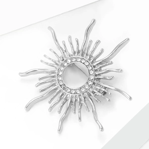 Detail of silver sunburst alloy brooch with sparkling rhinestones on a white stand