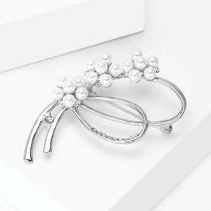 Détail d'une broche nœud argentée avec perles blanches et strass brillants sur fond